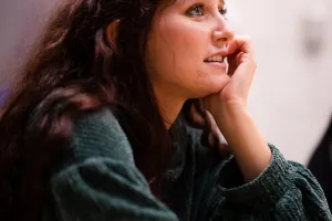 A student in a long sleeve green shirt has their hand under their chin and is intently watching a faculty member teach.