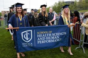 Students graduating holding an HSHP banner.