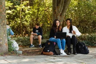 two students sit outdoors and look at a laptop screen together