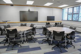 Classroom with tables and chairs on casters, computer monitors and large interactive display